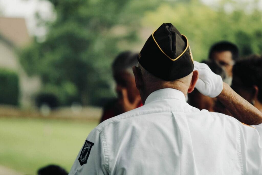 A military veteran wears his uniform and salutes, facing away from the camera.