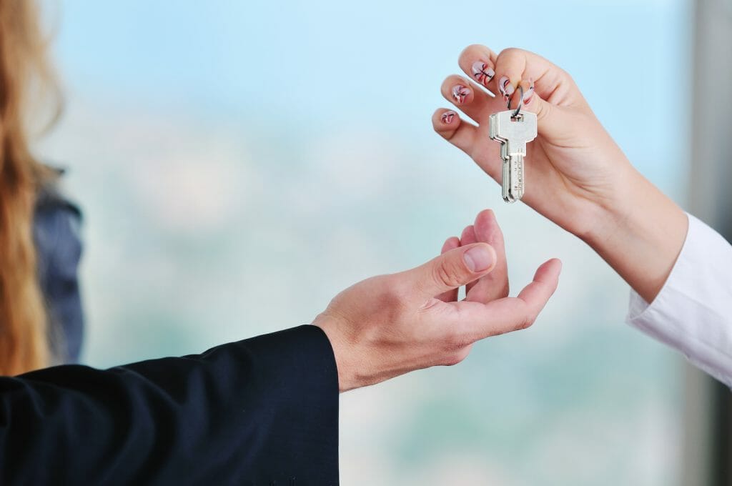 A close-up of two people exchanging house keys, symbolizing a real estate transaction