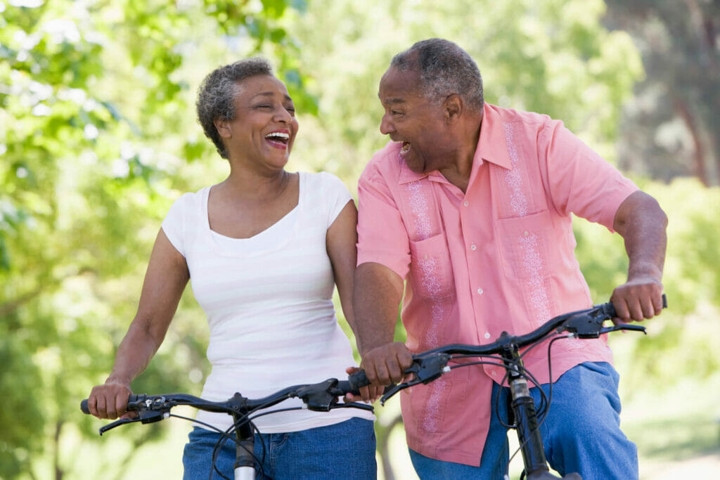 An older adult couple smile happily at each other as they ride bicycles