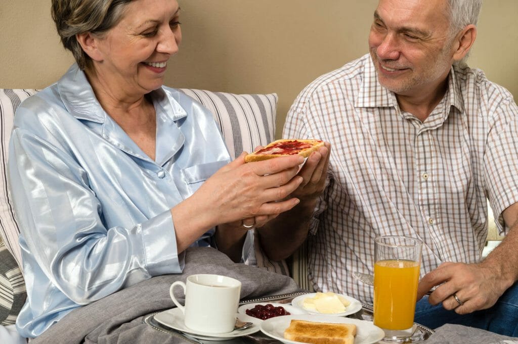 senior couple with the woman sitting in bed eating breakfast